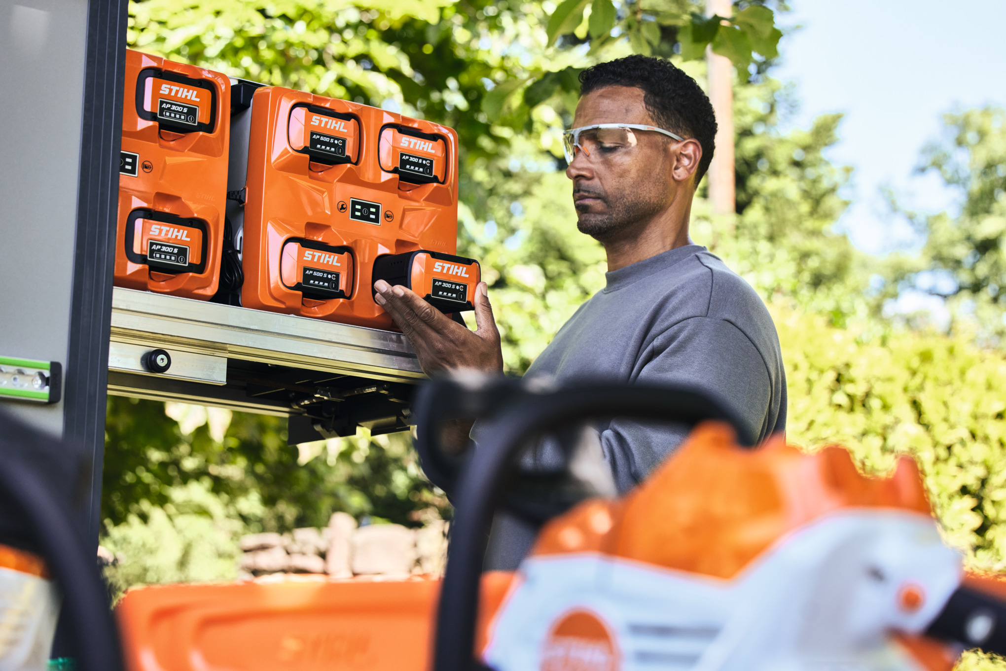 Un bărbat care poartă ochelari de protecție scoate un acumulator STIHL AP 300 S din bottTainer