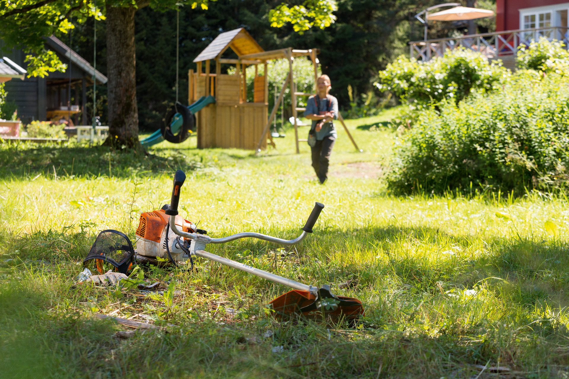 Motocoasa STIHL FS 240 se află în iarbă, iar pe fundal o femeie se pregătește pentru întreținere 