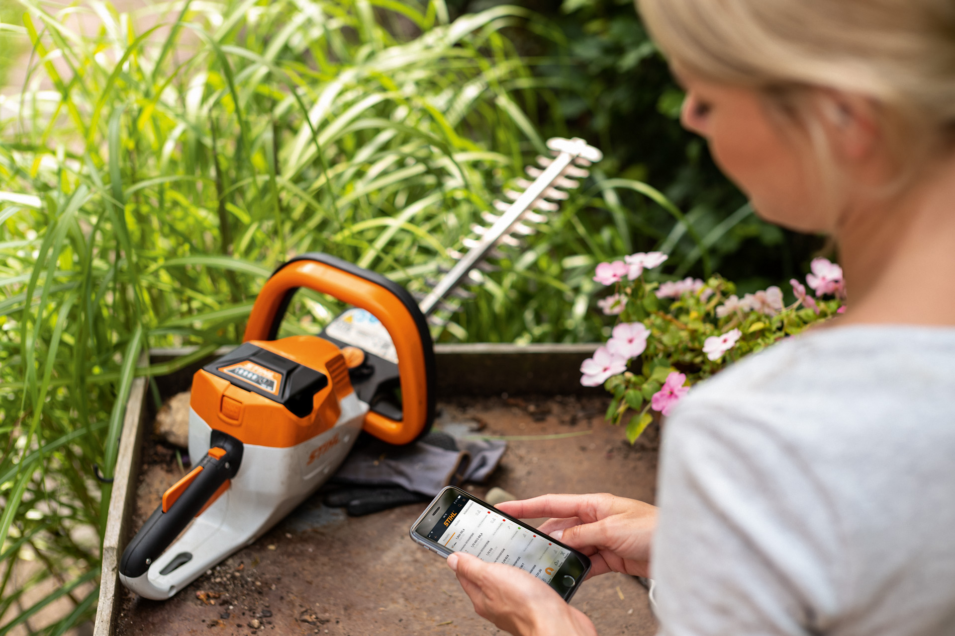 O femeie își înregistrează foarfeca de tuns garduri vii STIHL cu ajutorul aplicației STIHL de pe un smartphone