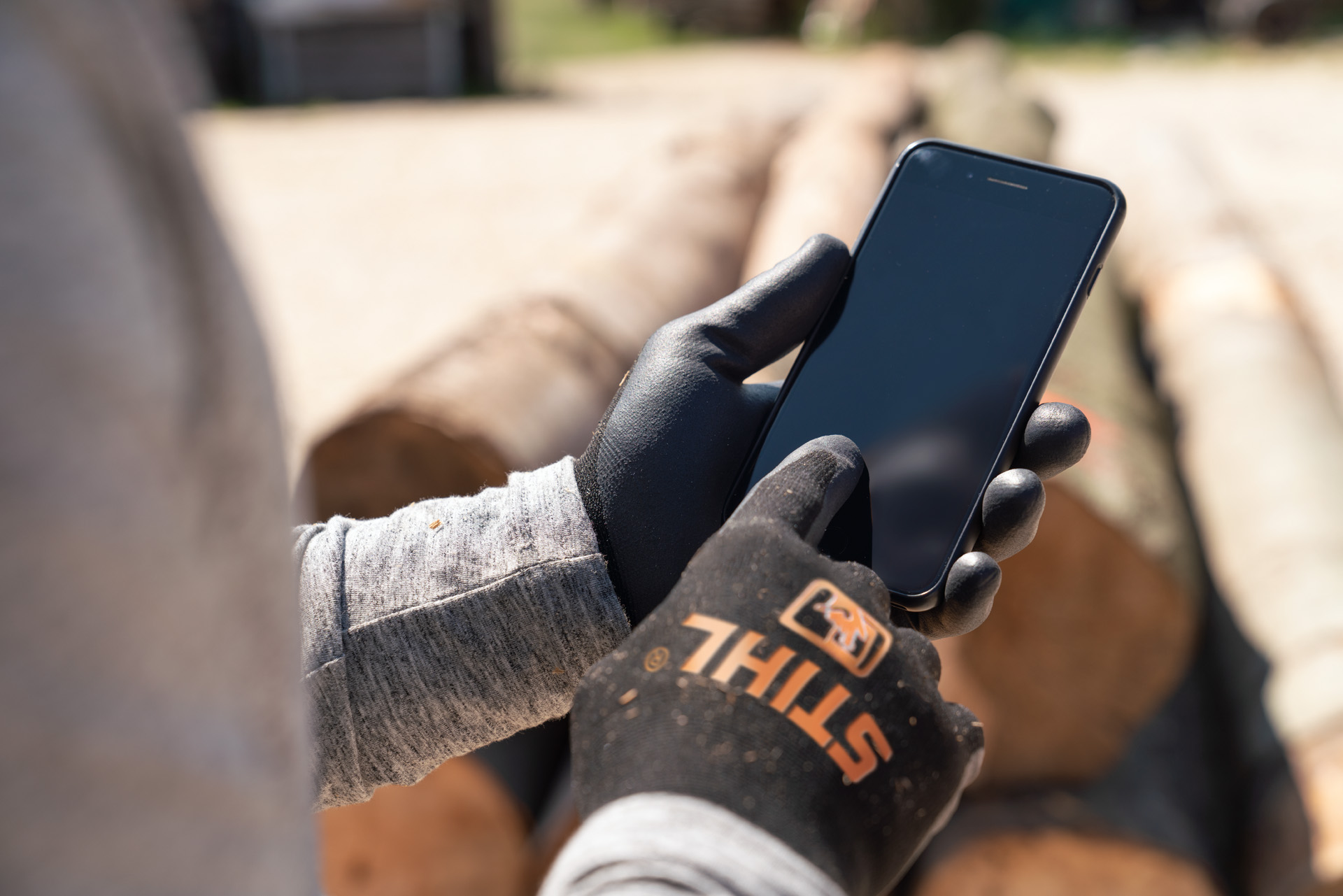 Un bărbat purtând mănuși de protecție care tastează pe smartphone-ul său.