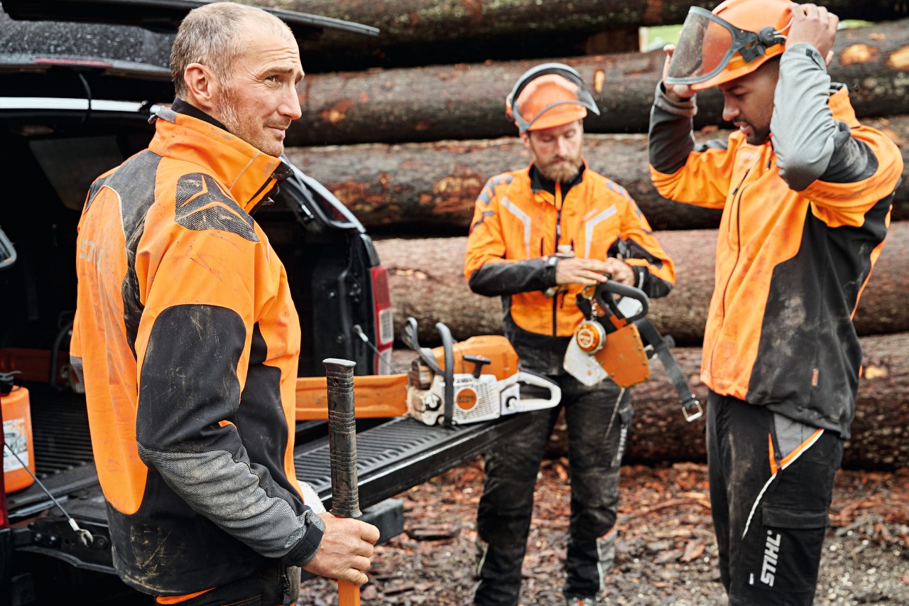 Trei bărbați îmbrăcați în echipament de protecție STIHL cu utilaje cu acumulator STIHL în fața zonei de încărcare a unei mașini