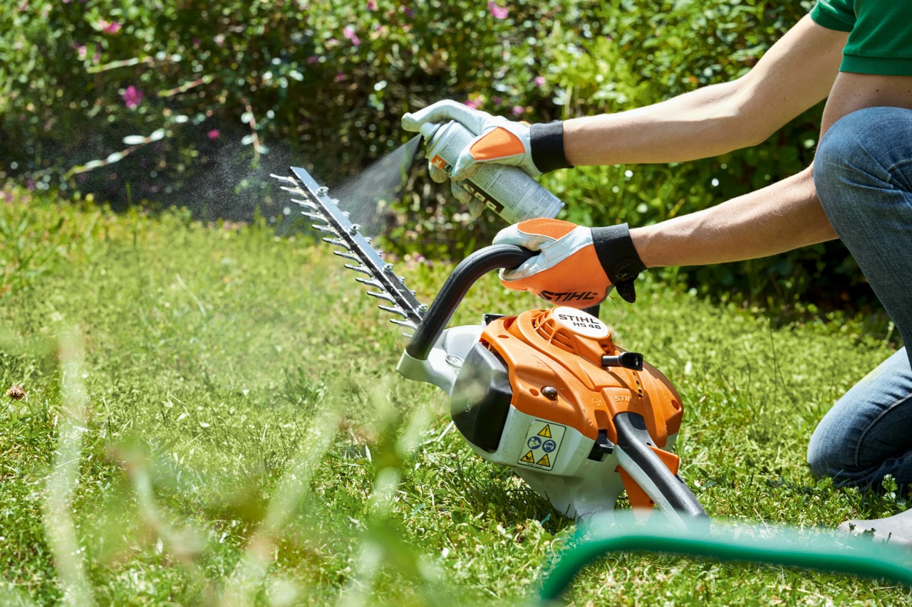  Foarfeca de tuns garduri vii pe benzină STIHL HS 82  T este pulverizată pe gazonul verde pentru a fi curățată