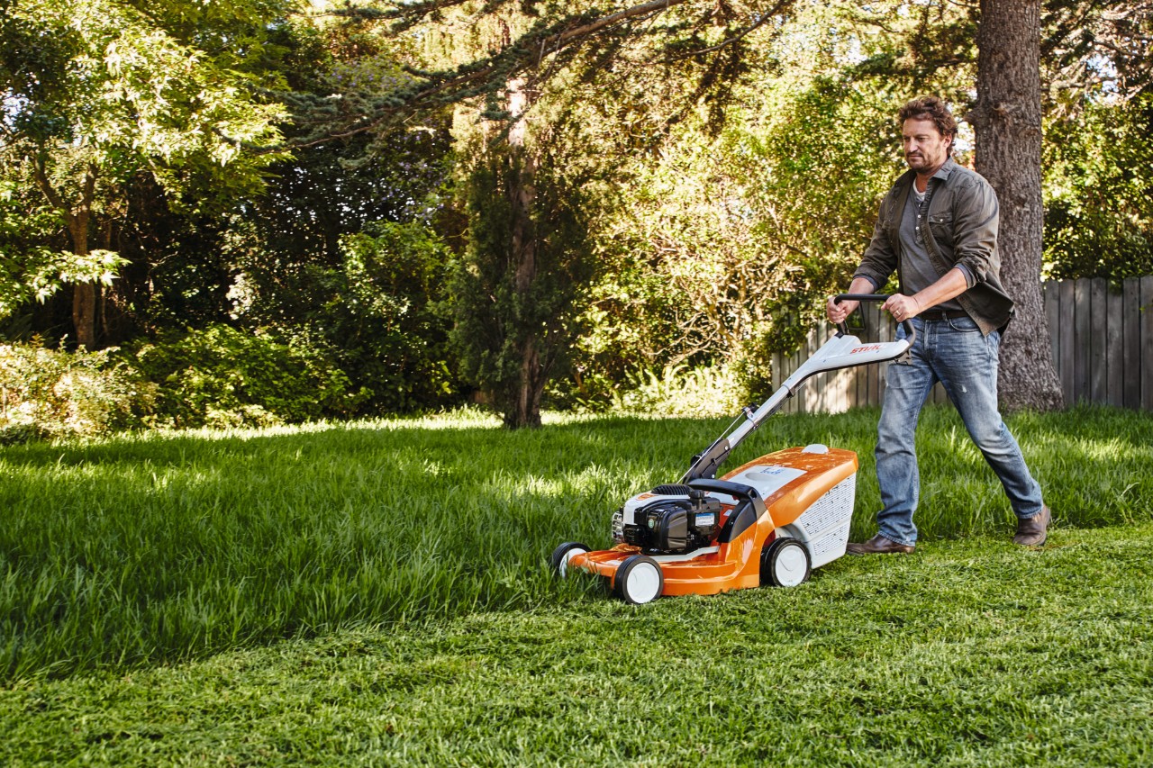 Un bărbat tunde gazonul într-o grădină cu o mașină de tuns iarba STIHL 