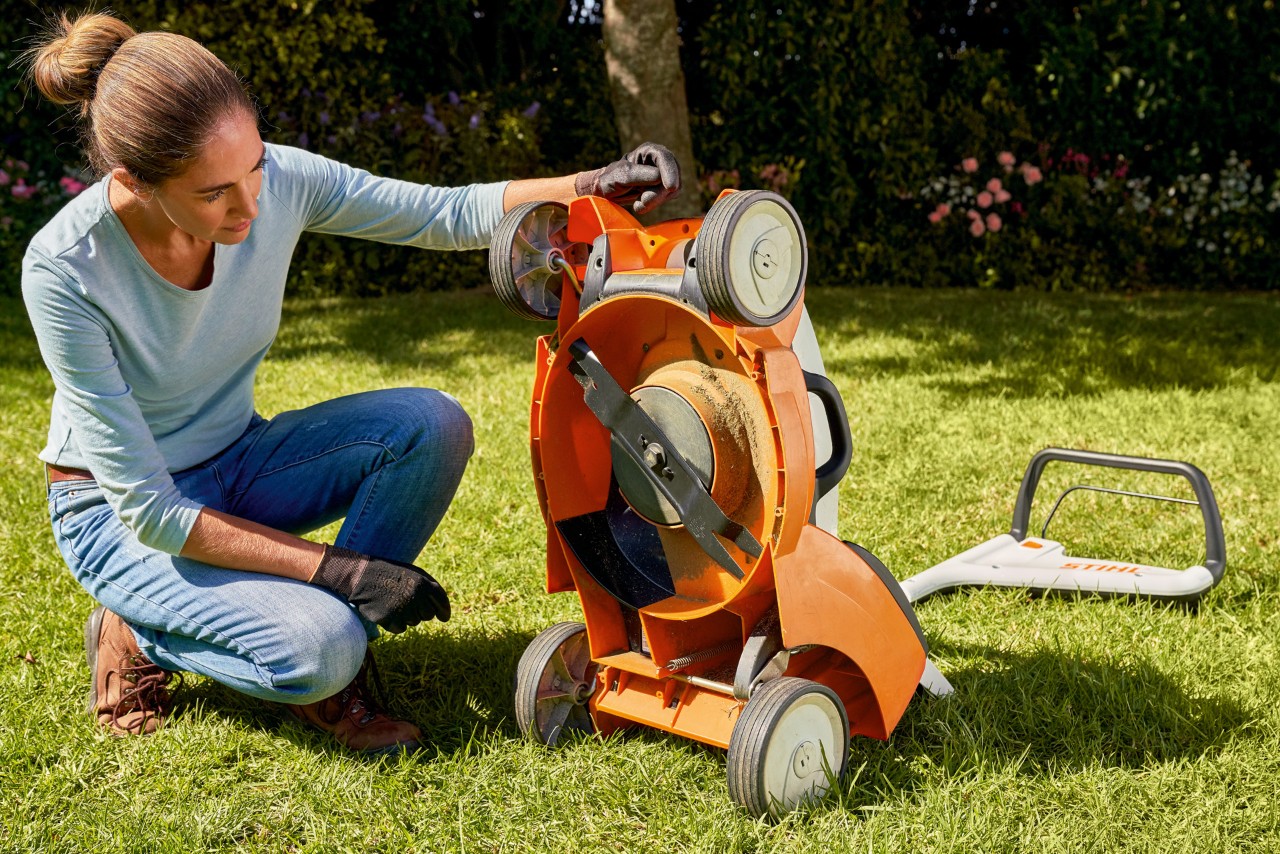 O femeie se uită în grădină sub mașina de tuns iarba cu acumulator STIHL RMA 339C