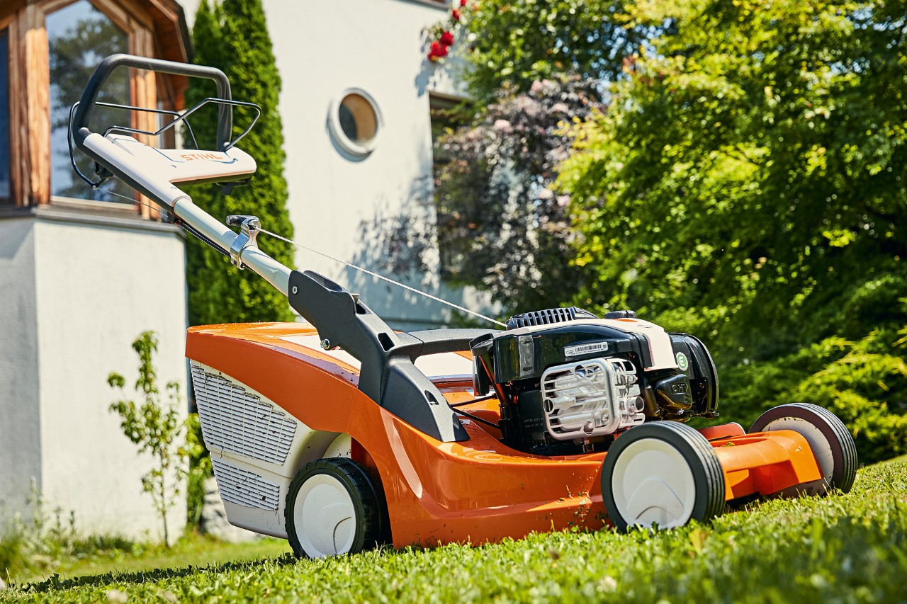Mașină de tuns iarbă pe benzină STIHL RM 443 T pe gazon verde în fața unei case 