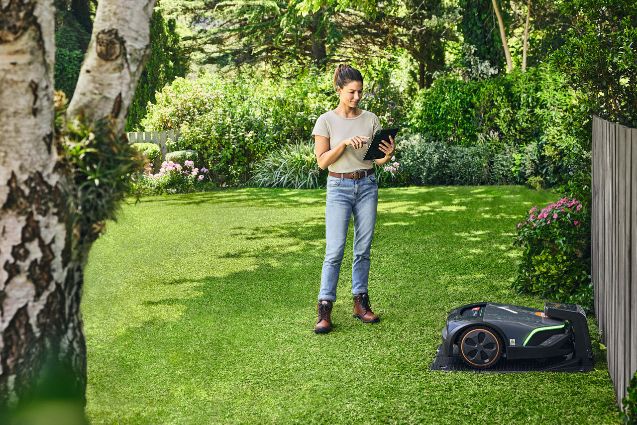 O femeie operează robotul STIHL iMOW® EVO prin intermediul unei tablete în grădina sa